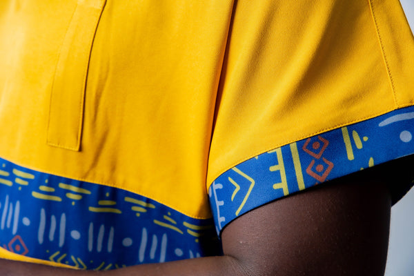 tunique médical homme jaune avec détails ethniques bleus, tenue professionnelle élégante twopikal wear , uniforme coloré caribéen infirmier ou aide soignante avec magnifique empiecement de motifs africains bleus.