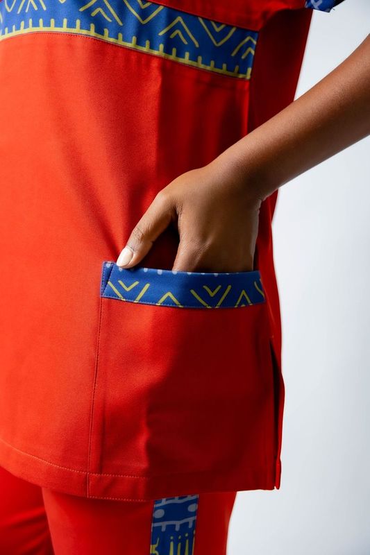 tunique médical femme rouge avec détails ethniques bleus, tenue professionnelle élégante twopikal wear , uniforme coloré caribéen infirmière ou aide soignante muni de jolies poches .