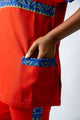 tunique médical femme rouge avec détails ethniques bleus, tenue professionnelle élégante twopikal wear , uniforme coloré caribéen infirmière ou aide soignante muni de jolies poches .